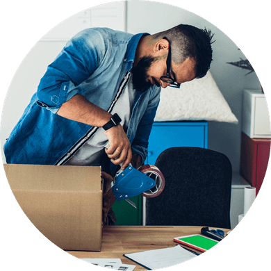 Bearded man taping up a usps shipping box on a wood table in a garage